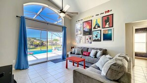 Ein geräumiges Wohnzimmer mit grauem Sofa, rotem Couchtisch und einem großen Fenster mit Blick auf einen Swimmingpool.