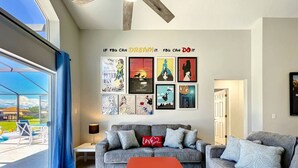 Ein Wohnzimmer mit grauem Sofa, einem roten Couchtisch und einer Wand, die mit Filmplakaten dekoriert ist.