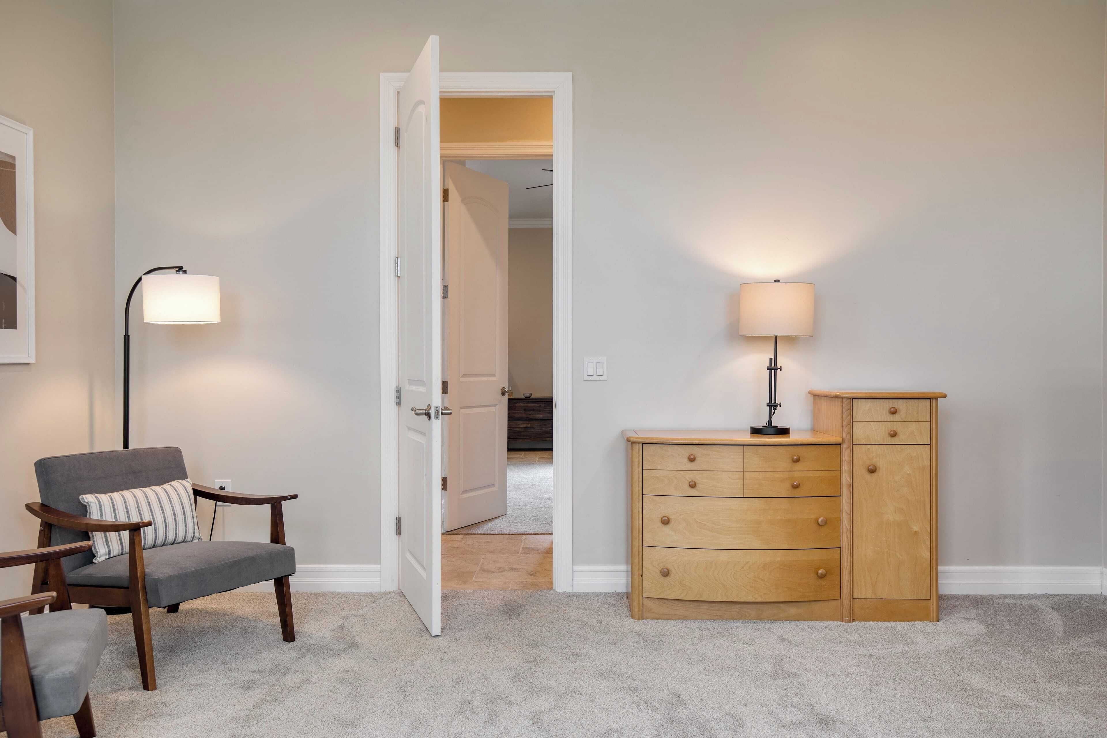 A room with a grey armchair, a wooden dresser, and a lamp.