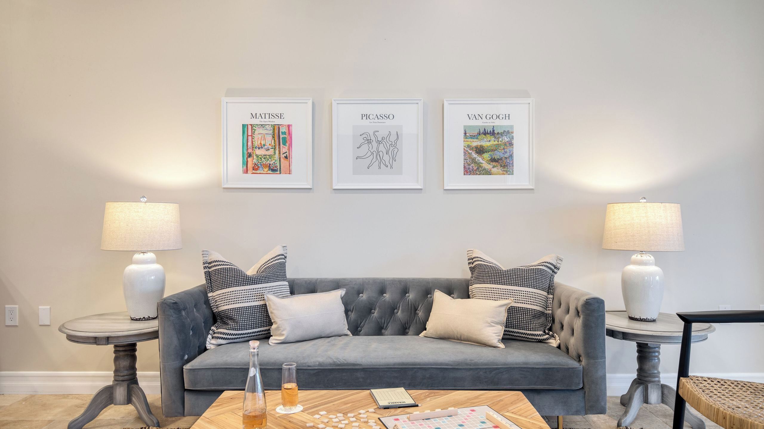 A living room with a grey sofa, two side tables with lamps, and three framed artworks on the wall.