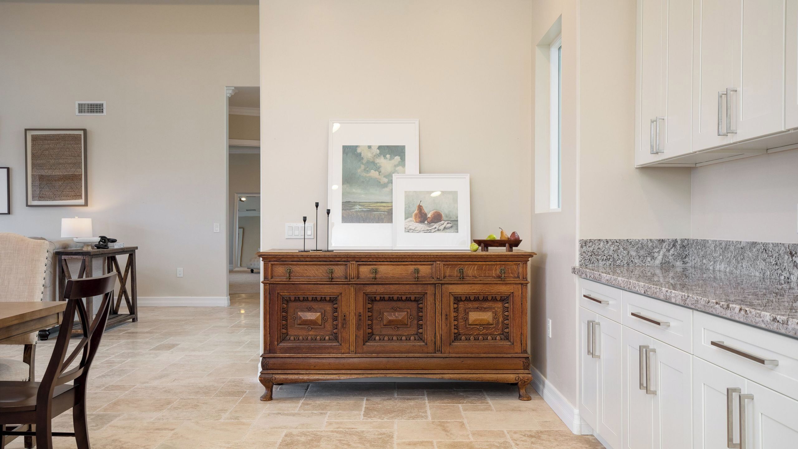 A kitchen with a wooden cabinet, a dining area with a table and chairs, and a framed picture on the wall.