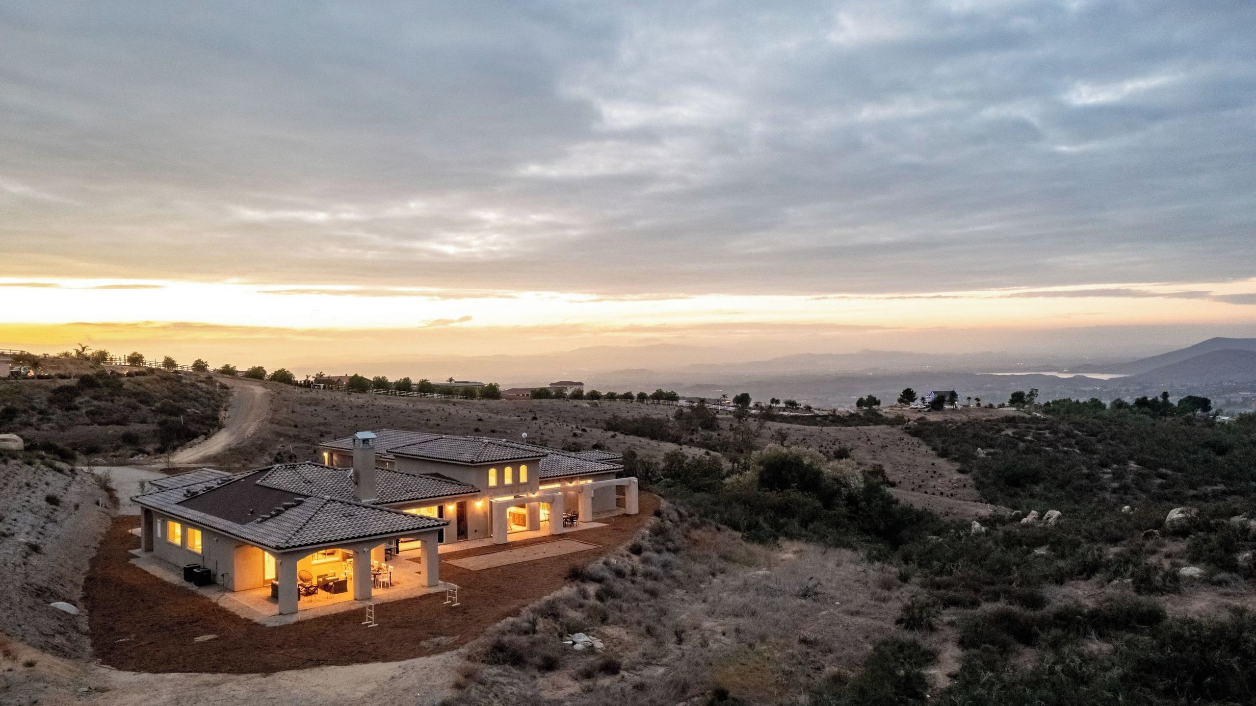 Uma casa moderna com um pátio, rodeada por uma paisagem montanhosa e vista para montanhas distantes.