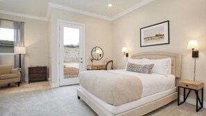 A bedroom with a large bed, a chair, a dresser, a door leading to a balcony, and a framed picture on the wall.