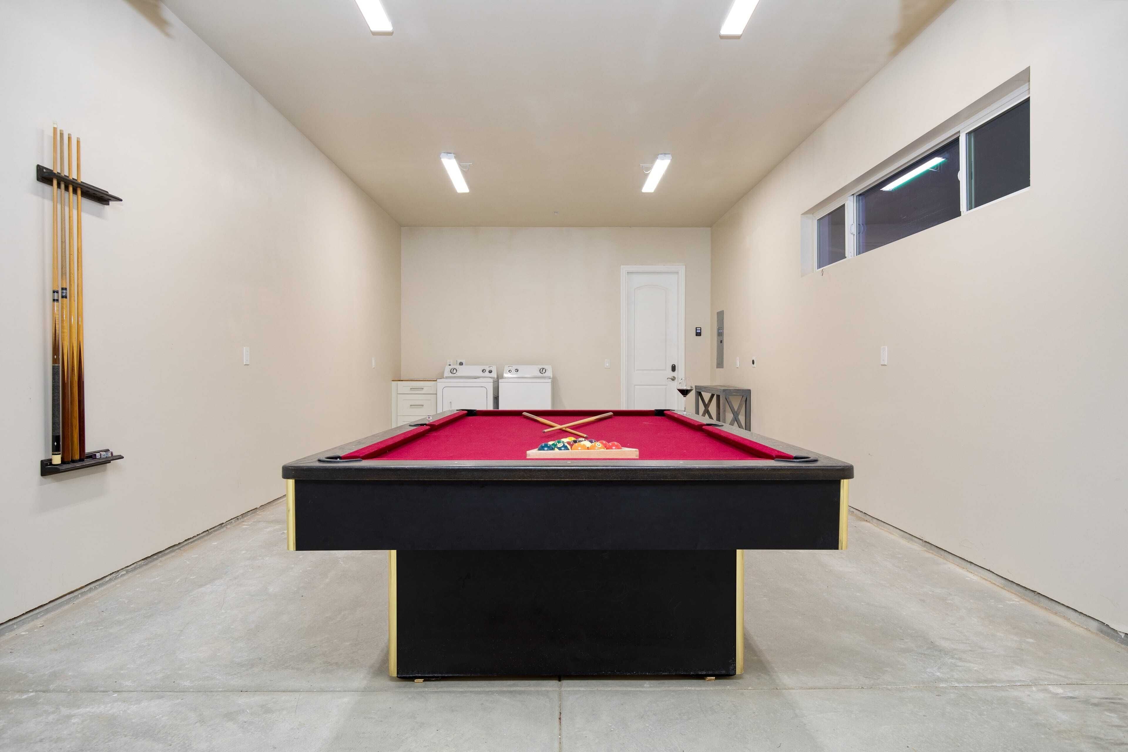 Una mesa de billar en una habitación con pared blanca, una puerta y una ventana.