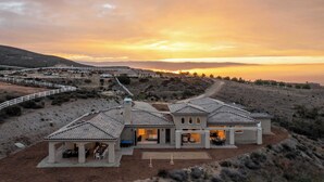 A large, modern house with multiple rooms and a patio area, surrounded by a fenced property and a scenic view of the landscape.
