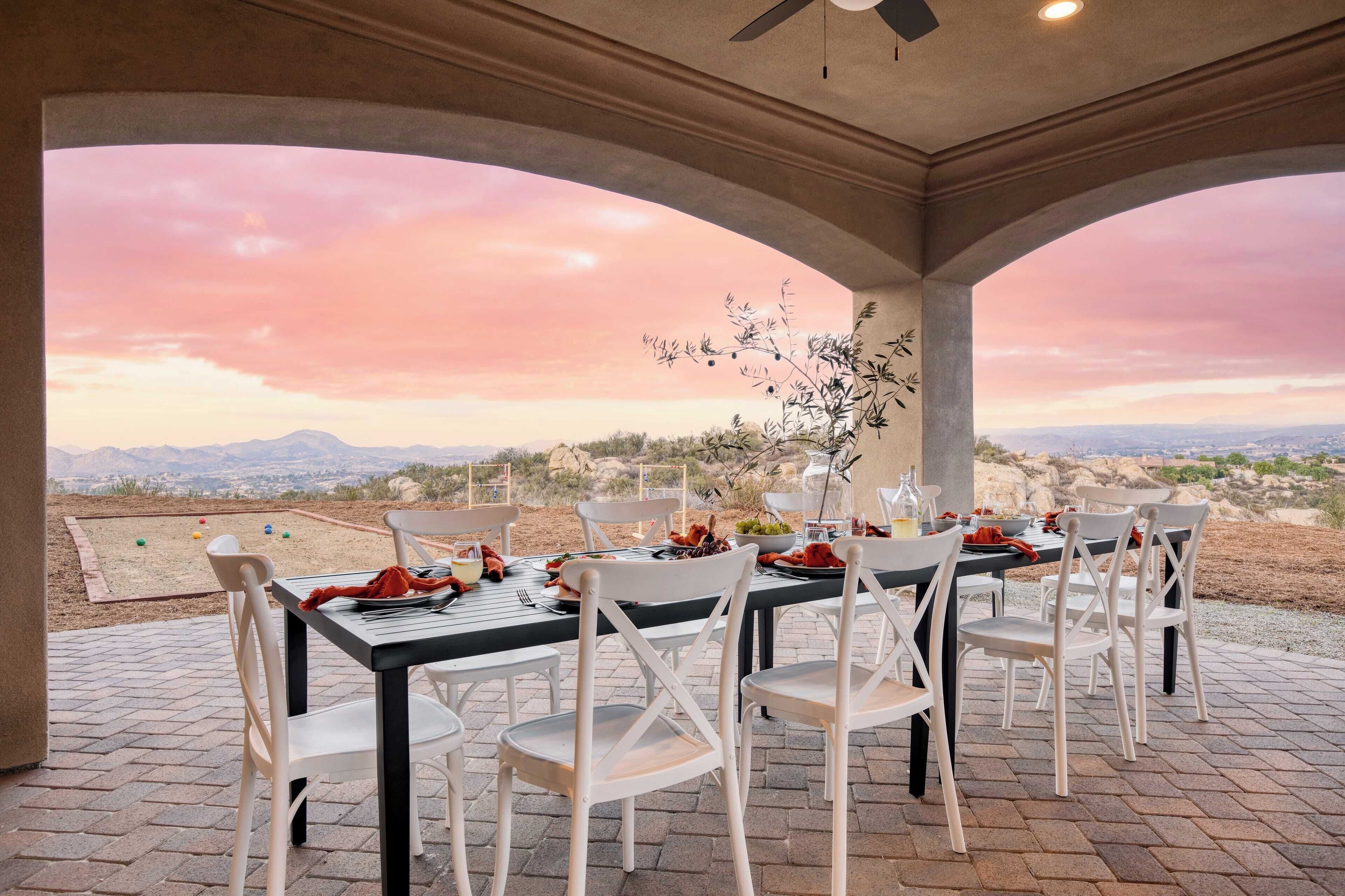 Un espace extérieur abrité, aménagé pour les repas, avec une table pour quatre personnes, offrant une vue panoramique sur un paysage magnifique, avec des montagnes et un coucher de soleil.