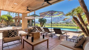 A covered outdoor seating area with lounge chairs, a wooden table, and striped umbrellas.