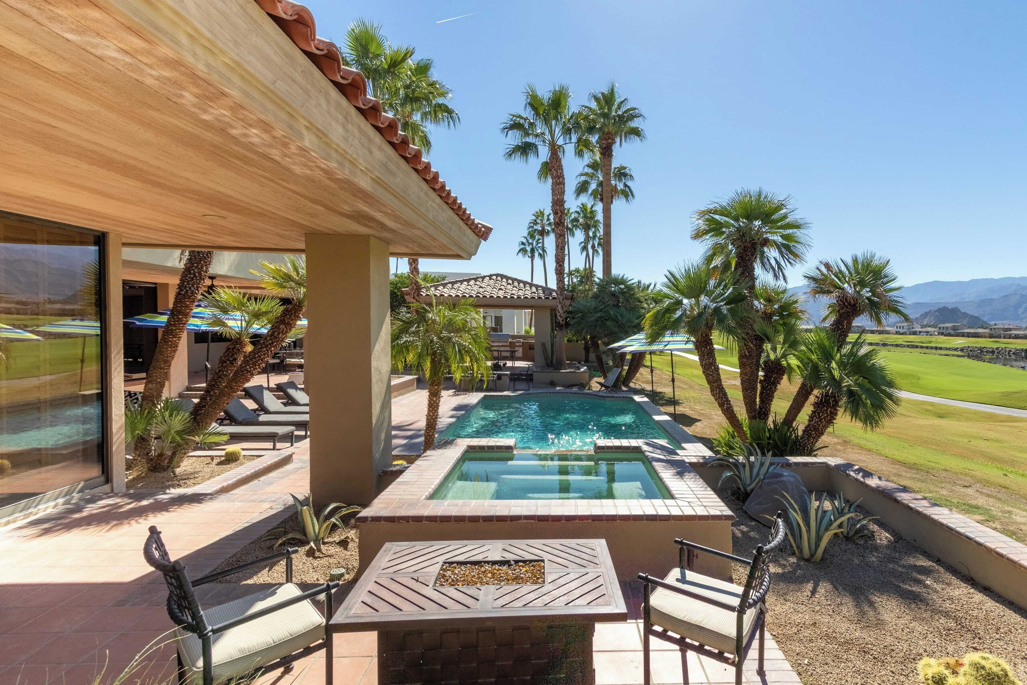 A pool area with lounge chairs, a table, and palm trees.