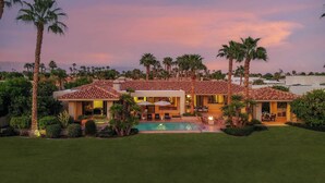 A modern house with a swimming pool, surrounded by palm trees and a well-maintained lawn.
