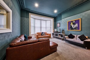 Un salón con un sofá de cuero marrón, un sofá estampado y un televisor sobre un mueble.