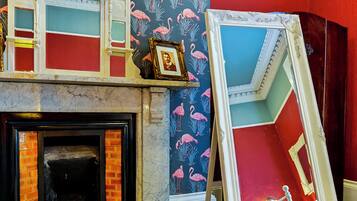 A room with a fireplace, a mirror, and a wall with a flamingo pattern.