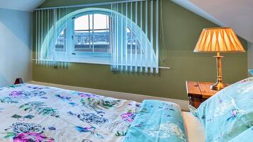 A bedroom with a bed, a window with curtains, a lamp, and a view of the city.