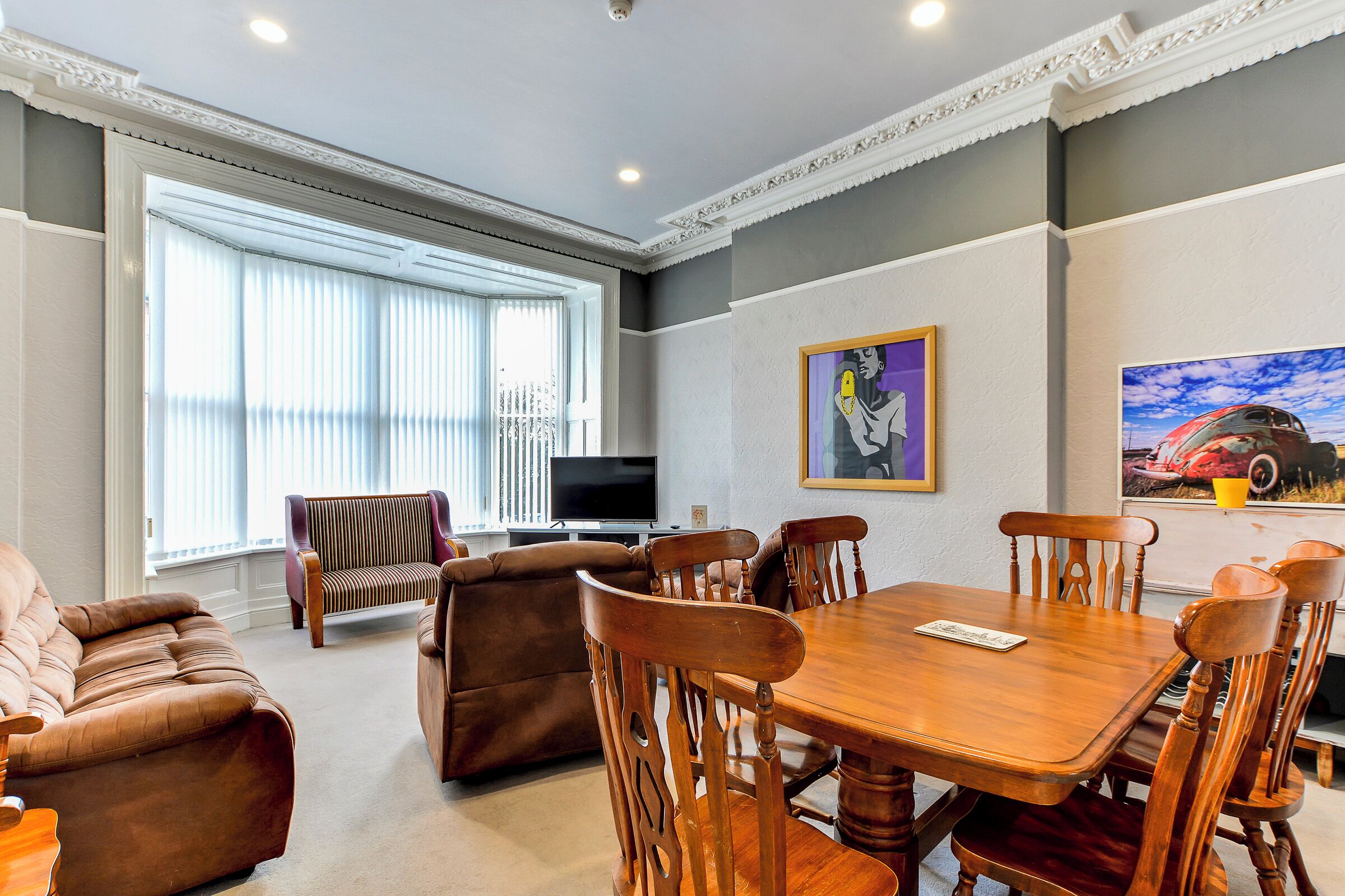 Un salón amplio con una mesa de comedor de madera, sofás cómodos y un gran ventanal con persianas.