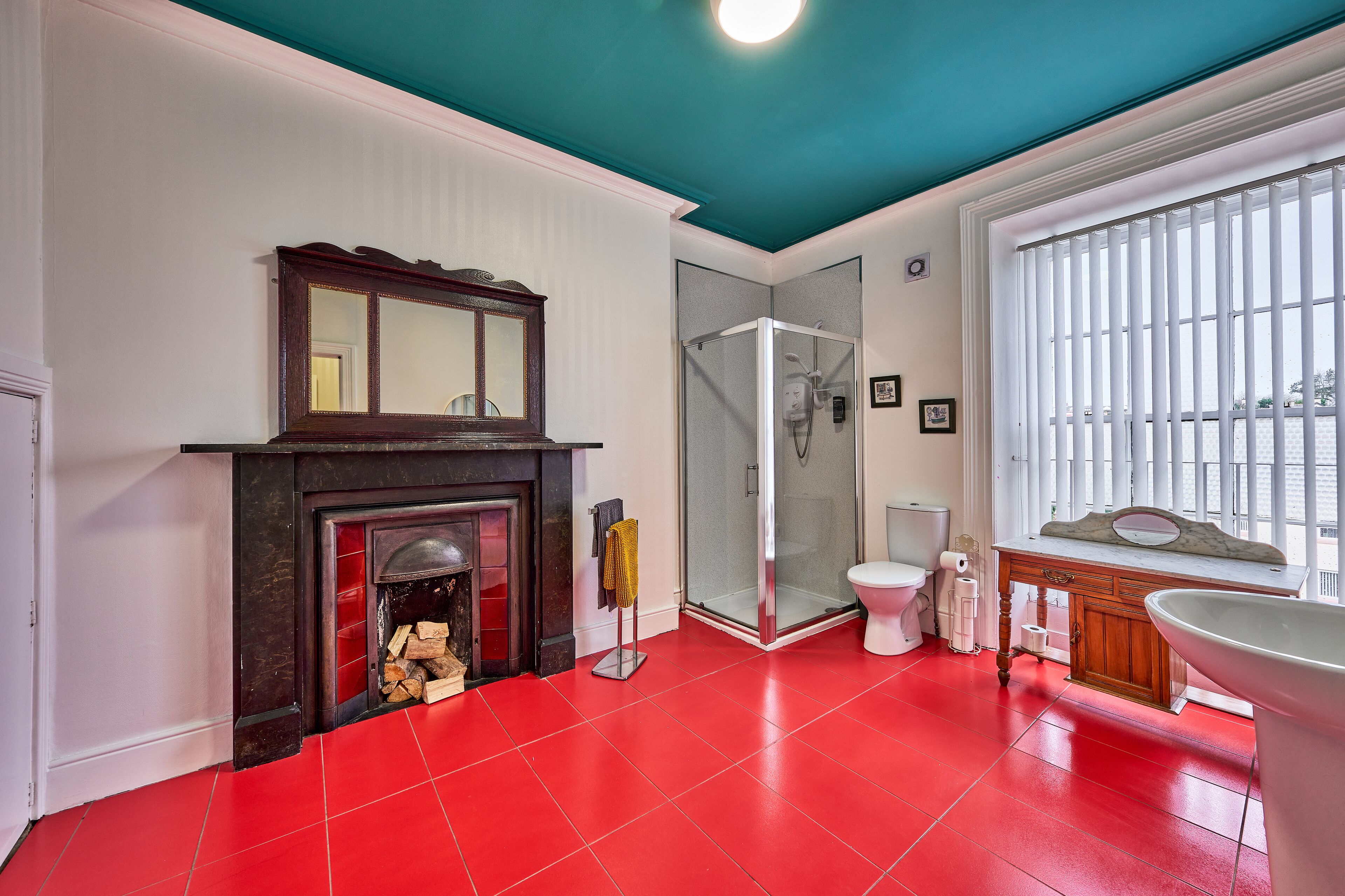 A bathroom with a red floor, a white toilet, a glass shower enclosure, and a white sink with a marble countertop.