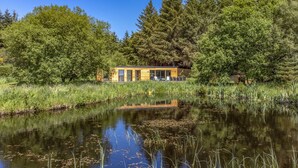 Eine moderne Hütte mit Glastür, umgeben von dichtem Wald und einem Teich.