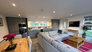 Ein modernes Wohnzimmer mit einem grauen Ecksofa, einem Holzesstisch und einer Küche im Hintergrund.
