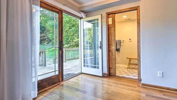 Una habitación con piso de madera, una puerta corredera de vidrio que da a una terraza y una puerta de madera a otra habitación.