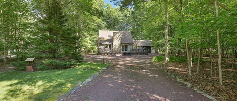 A house surrounded by a forested area with a gravel path leading to the entrance.