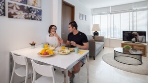 A modern living room with a dining area, featuring a sofa, a coffee table, and a TV displaying 'PITBULL SONGS'. - THE PENTHOUSE KLCC (Kuala Lumpur)