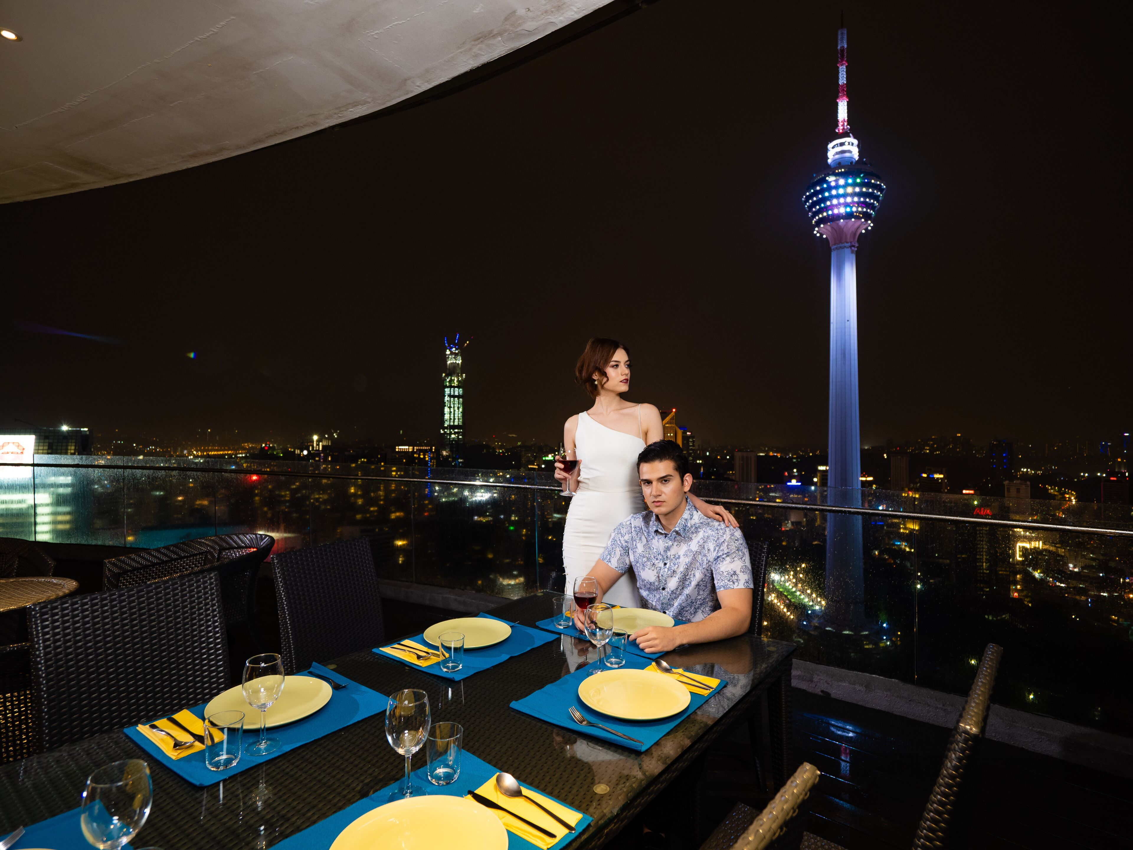 A rooftop dining area with a city skyline view, including a prominent tower.