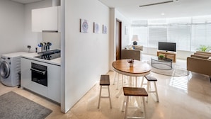 A modern kitchen with built-in appliances, a dining area with stools, and a living room with a TV and sofa. - THE PENTHOUSE KLCC (Kuala Lumpur)