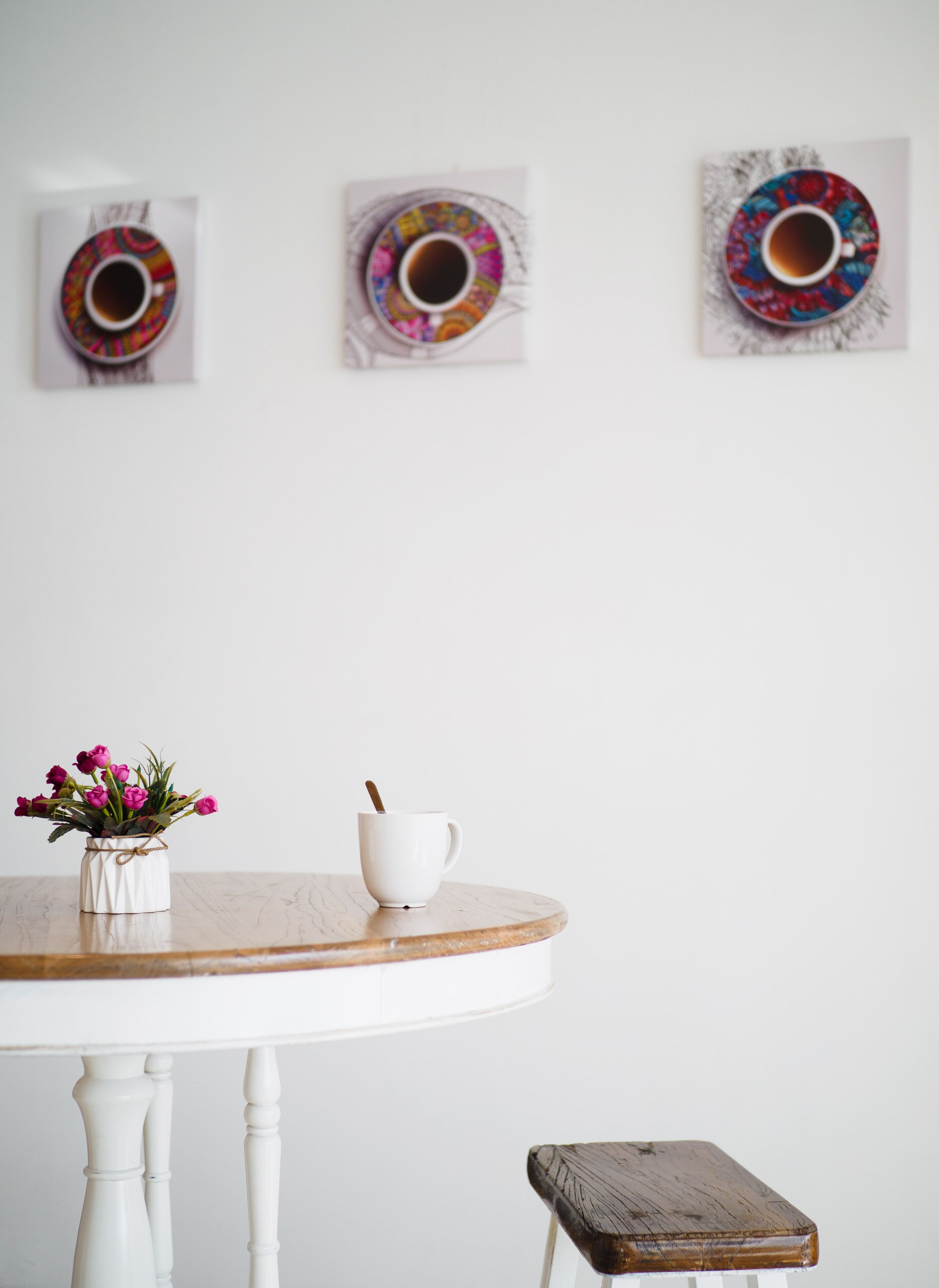 A round wooden table with a white cup and a small white vase with pink flowers.