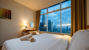 A hotel room with a large bed, a desk with a lamp, a chair, and a view of a cityscape through large windows. - THE PENTHOUSE KLCC (Kuala Lumpur)