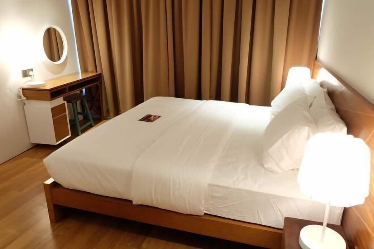 A neatly made bed with white linens, a bedside lamp, a small table with a mirror, and a wooden headboard.