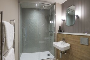 Een moderne badkamer met een douche in een glazen cabine, een wit wastafeltje en een houten wastafelmeubel.