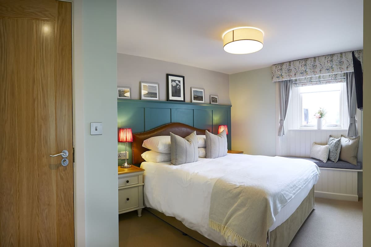 Un dormitorio ordenado con una cama grande, lámparas de noche, una ventana con cortinas e imágenes enmarcadas en la pared.