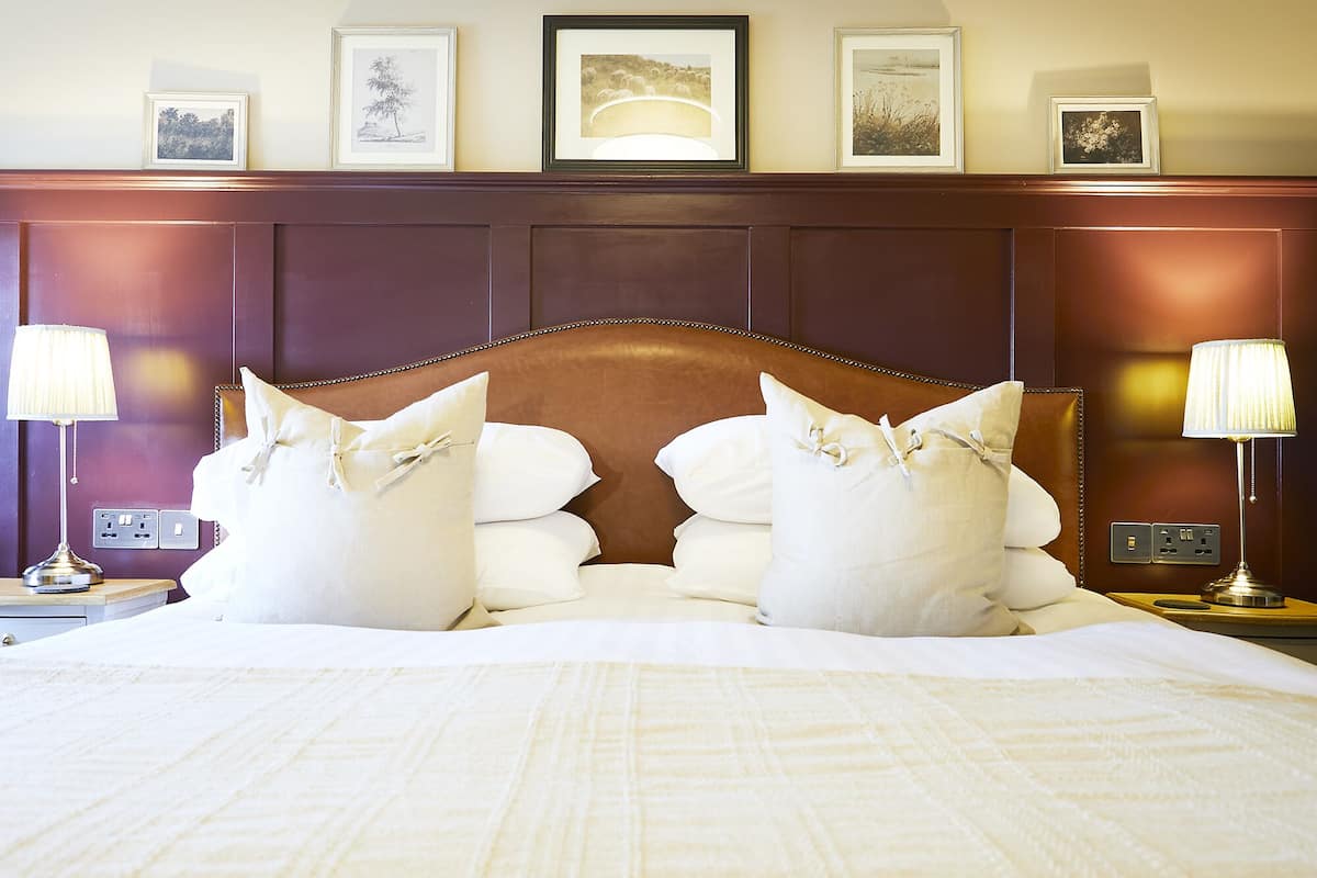 Una cama bien hecha con sábanas blancas y almohadones decorativos, un cabecero de madera y cuadros en la pared de arriba.