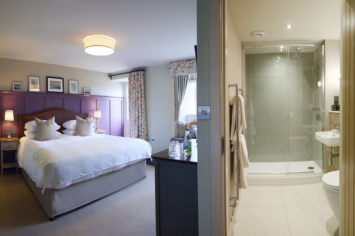 Un dormitorio con cama, mesitas de noche y velador. Hay un baño con ducha, lavamanos e inodoro.