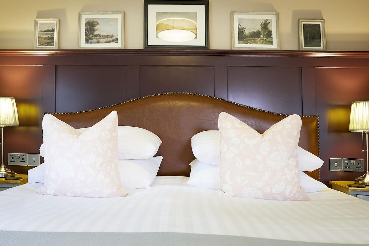 Una cama bien tendida con almohadillas de estampado floral, un cabecero de madera y cuadros enmarcados en la pared superior.