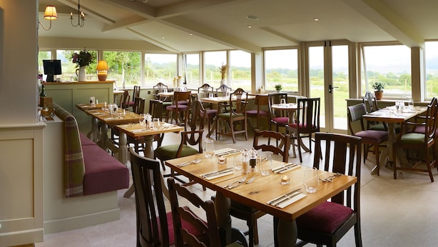 A restaurant with multiple dining tables and chairs, large windows offering a view of the outdoors, and a cozy seating area with a sofa. - The Grainary Boutique Hotel (Scarborough)