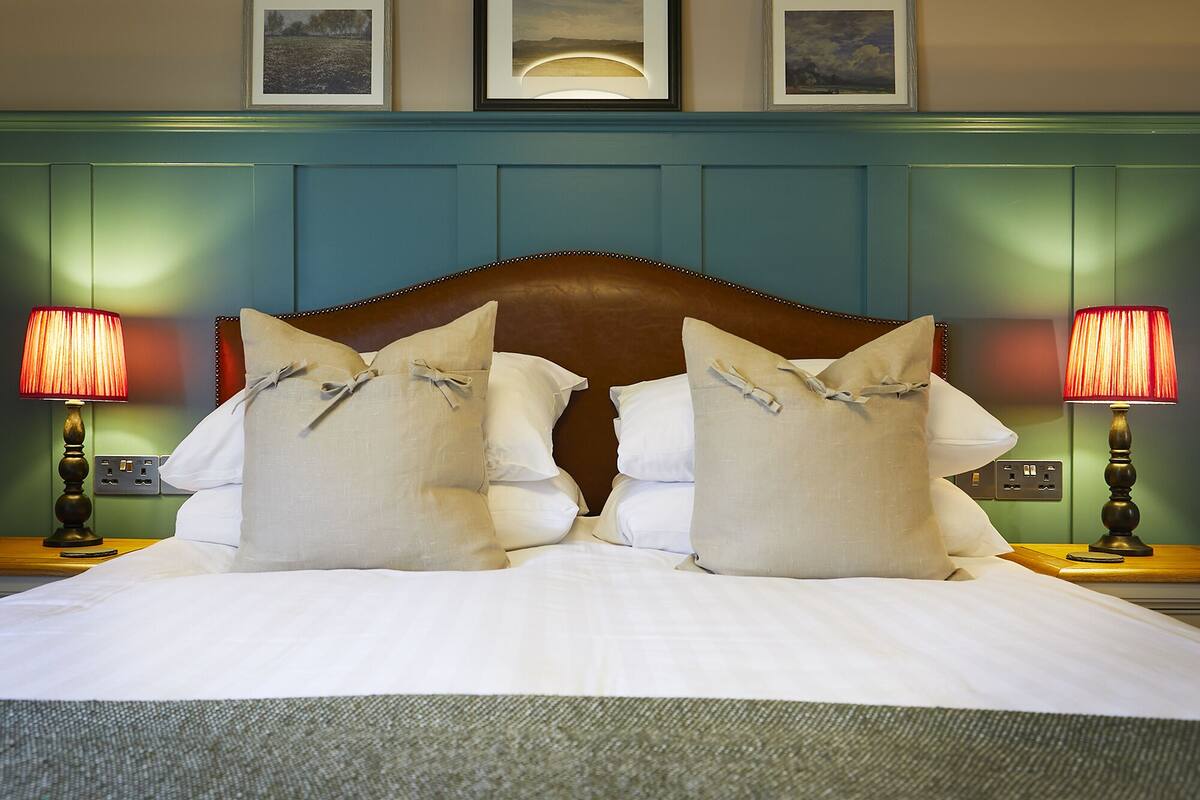 Una cama bien hecha con sábanas blancas y almohadones decorativos, con dos lámparas de noche a cada lado.