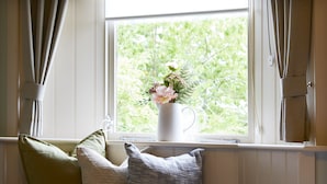 A window with a white vase containing flowers, two pillows on a bench, and curtains on either side. - The Grainary Boutique Hotel (Scarborough)