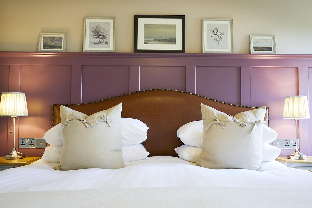 Una cama bien tendida con sábanas blancas y almohadas decorativas, un cabecero de madera y cuadros en la pared.