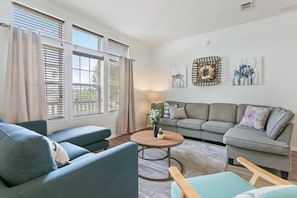 Ein Wohnzimmer mit grauem Sofa, blauem Sessel, rundem Holztisch und grauer Couch.