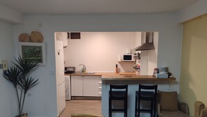 Cocina compacta con cubierta de madera, un microondas y un lavamanos. En la zona de comedor contigua, hay dos sillas y una mesa.
