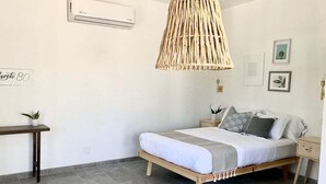 A bedroom with a bed, bedside tables, a hanging light fixture, and a small table. - Loreto80– Studio Palo Blanco (Loreto)