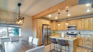 A modern kitchen with wooden cabinets, stainless steel appliances, and a bar area with stools. - The View at Mountain Retreat By Red Rocks & Golden (Evergreen)