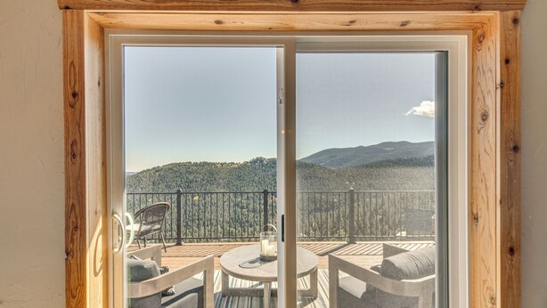 A balcony with a wooden frame, a table with a candle, and a view of a forested mountain range. - The View at Mountain Retreat By Red Rocks & Golden (Evergreen)