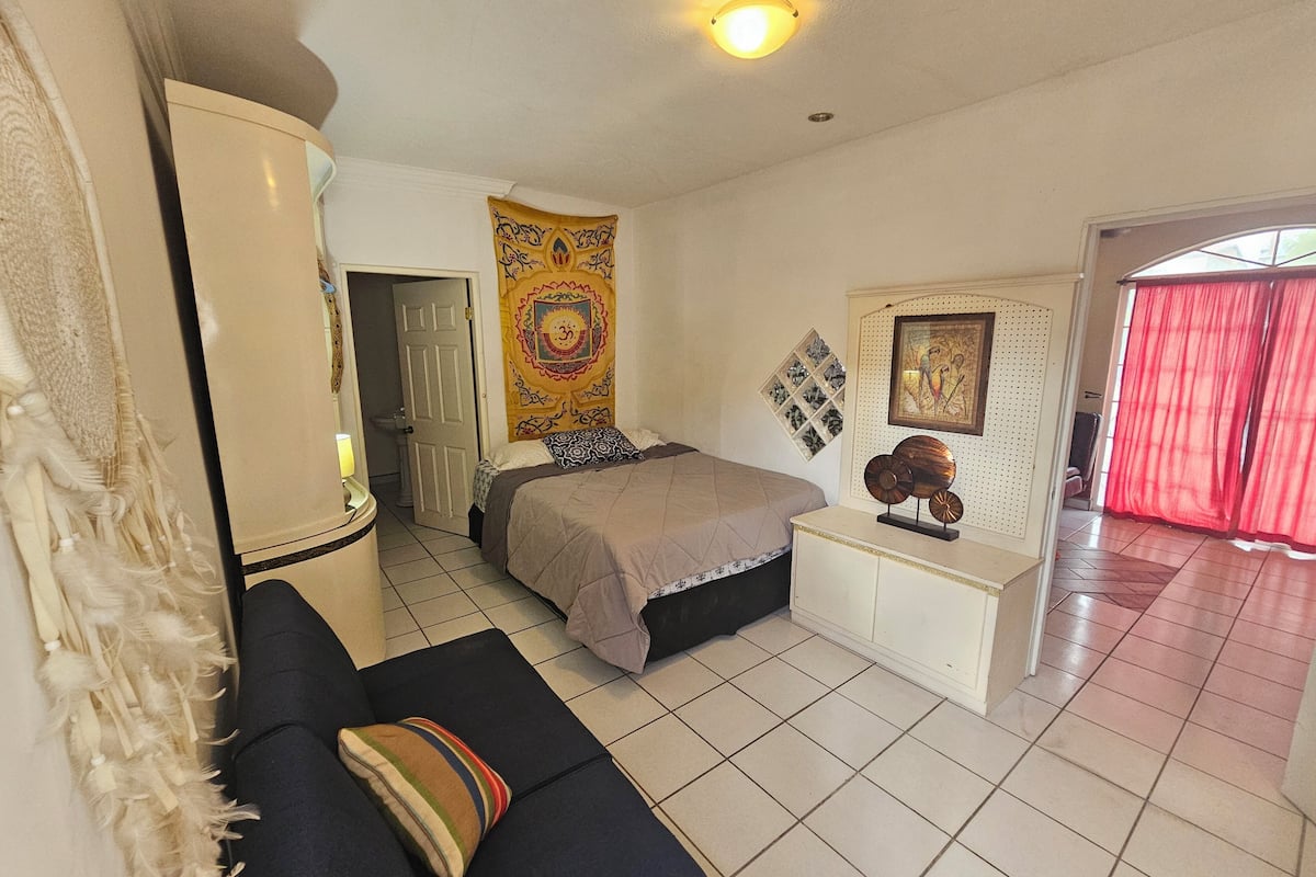 A bedroom with a bed, a sofa, a bedside table, a tapestry, and a wall-mounted picture.