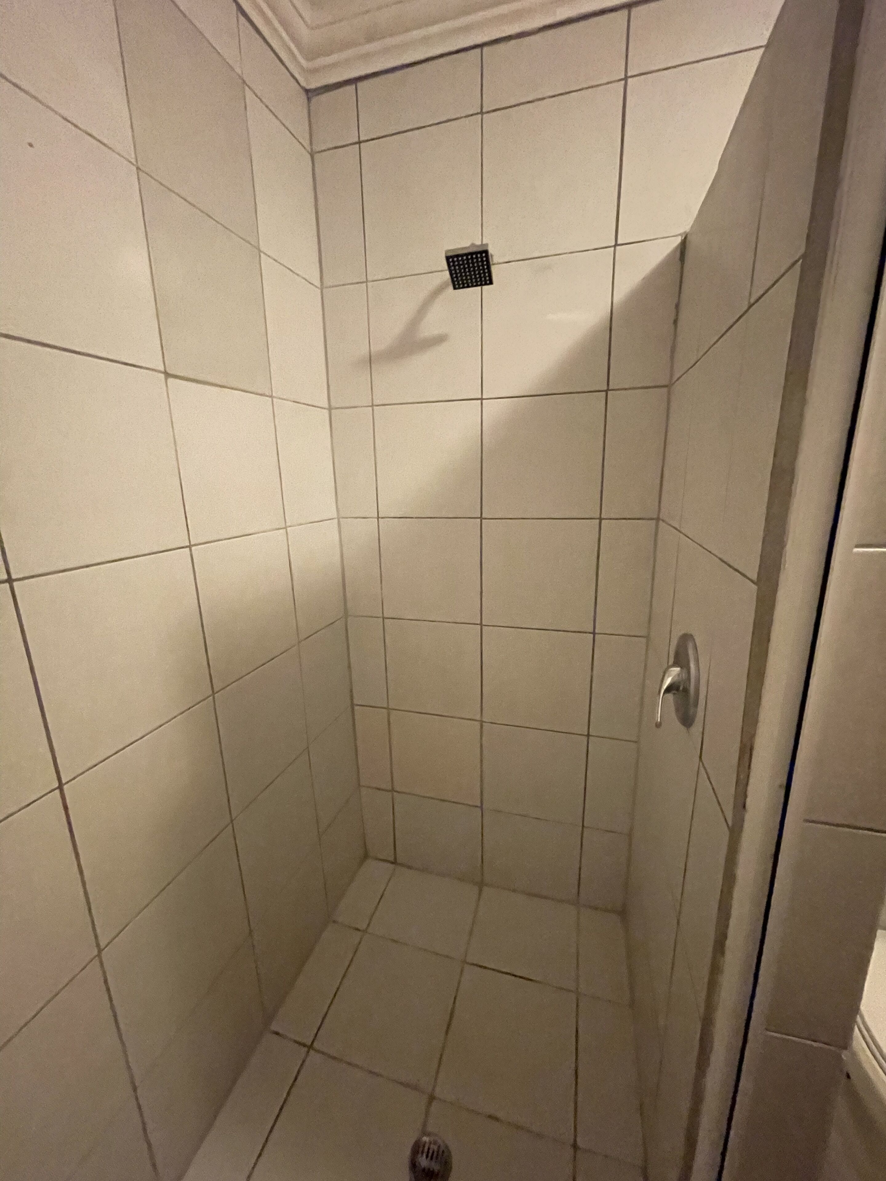 Ein kleines Duschbad mit Fliesen, einer Tür und einem Lüftungsgitter.