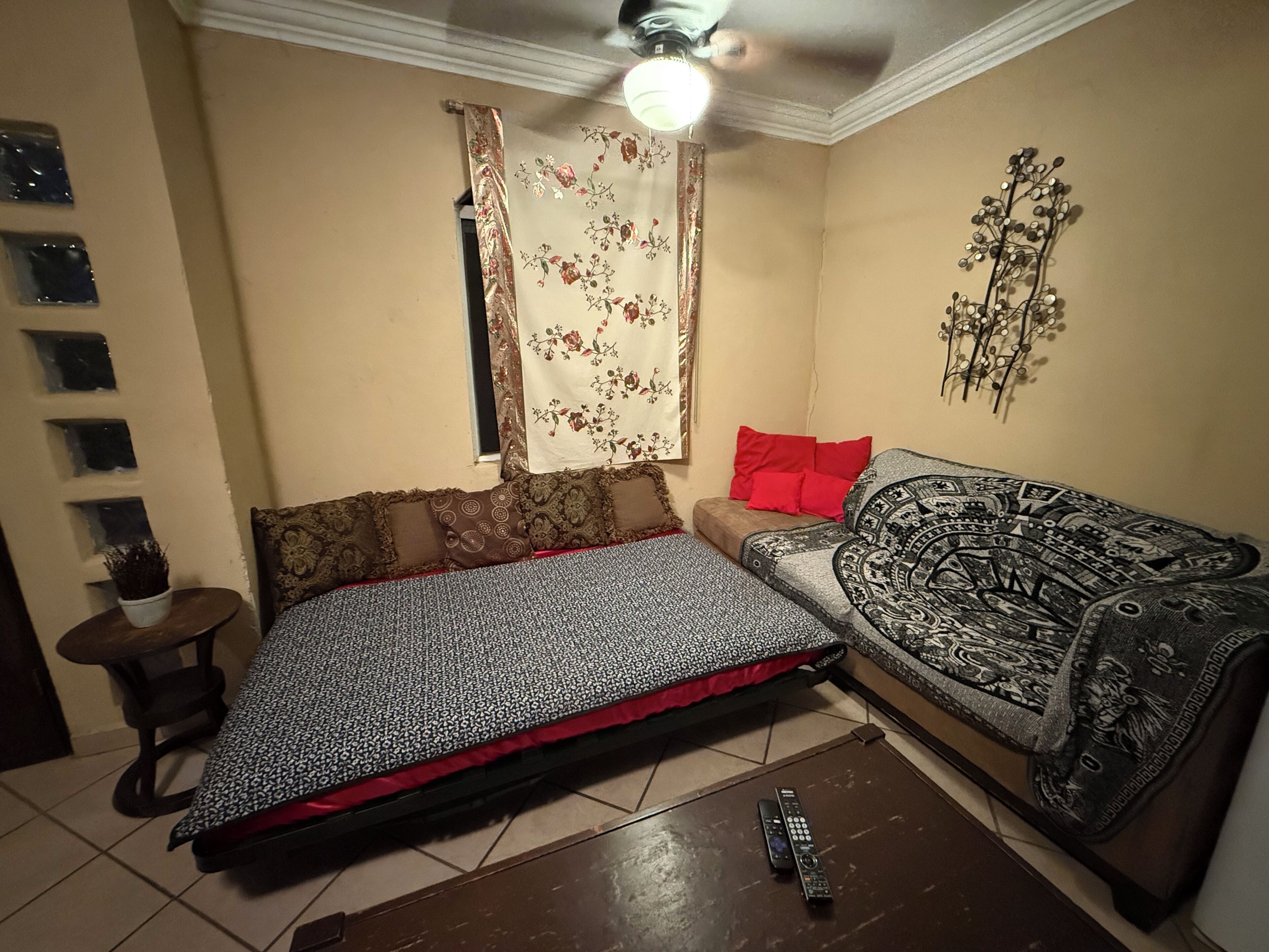 Una sala pequeña con sofá, cama, ventilador de techo y un adorno en la pared.