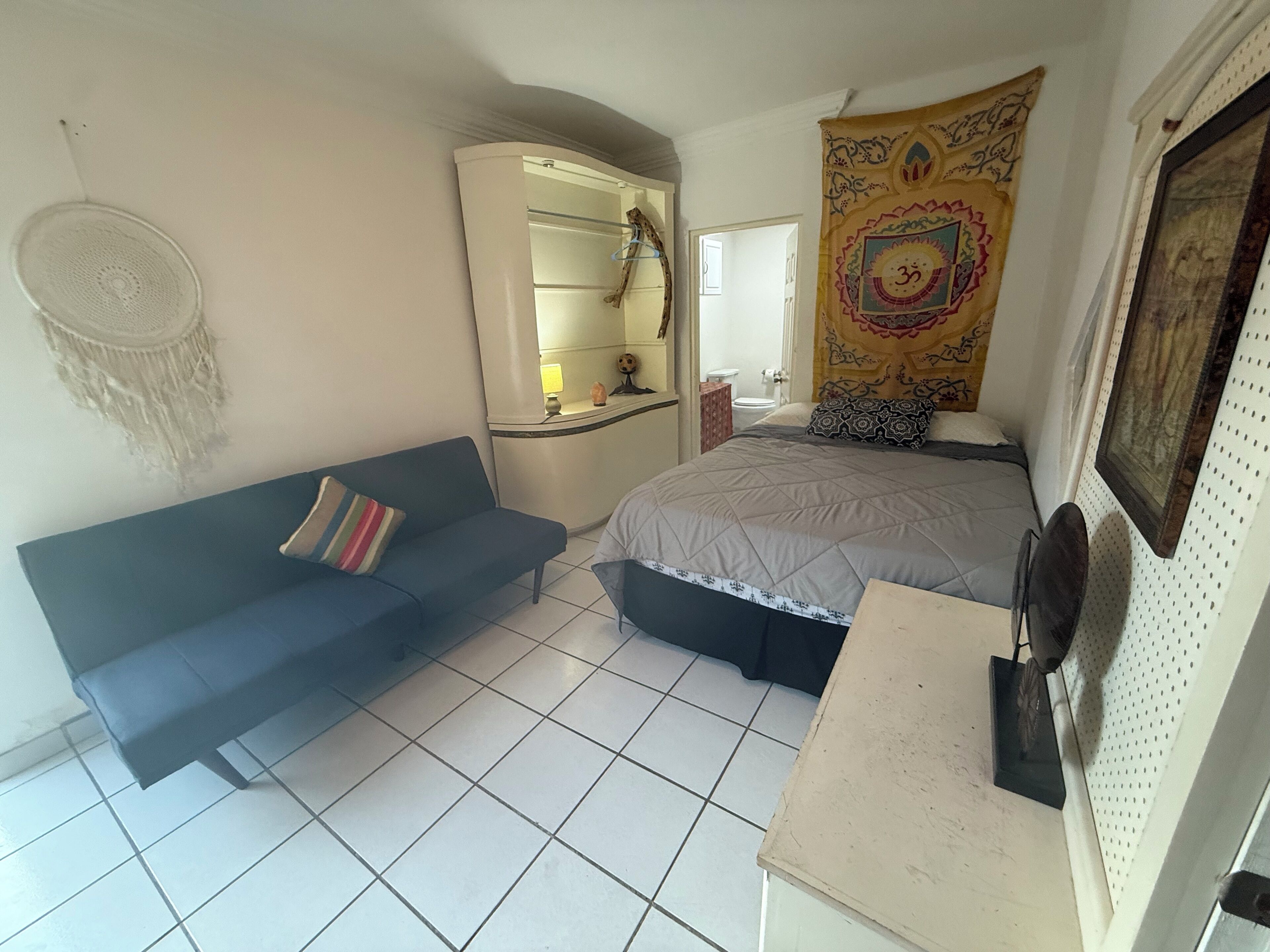 Un dormitorio con una cama, un sofá azul, una mesita, un armario y un tapiz.