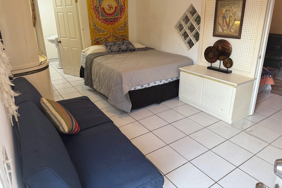 A bedroom with a bed, a sofa, a nightstand, a wall tapestry, and a wall-mounted picture.