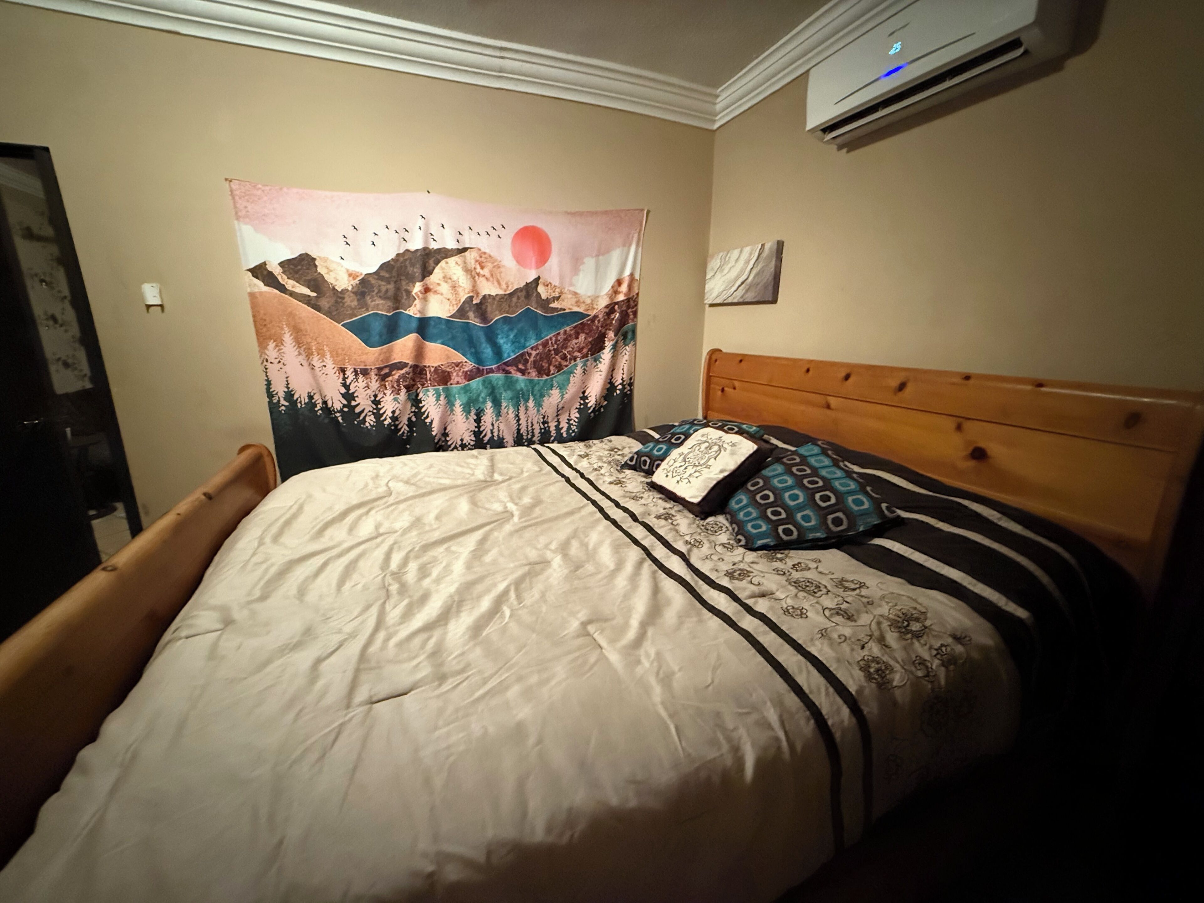 A bedroom with a bed, a tapestry, and an air conditioning unit.