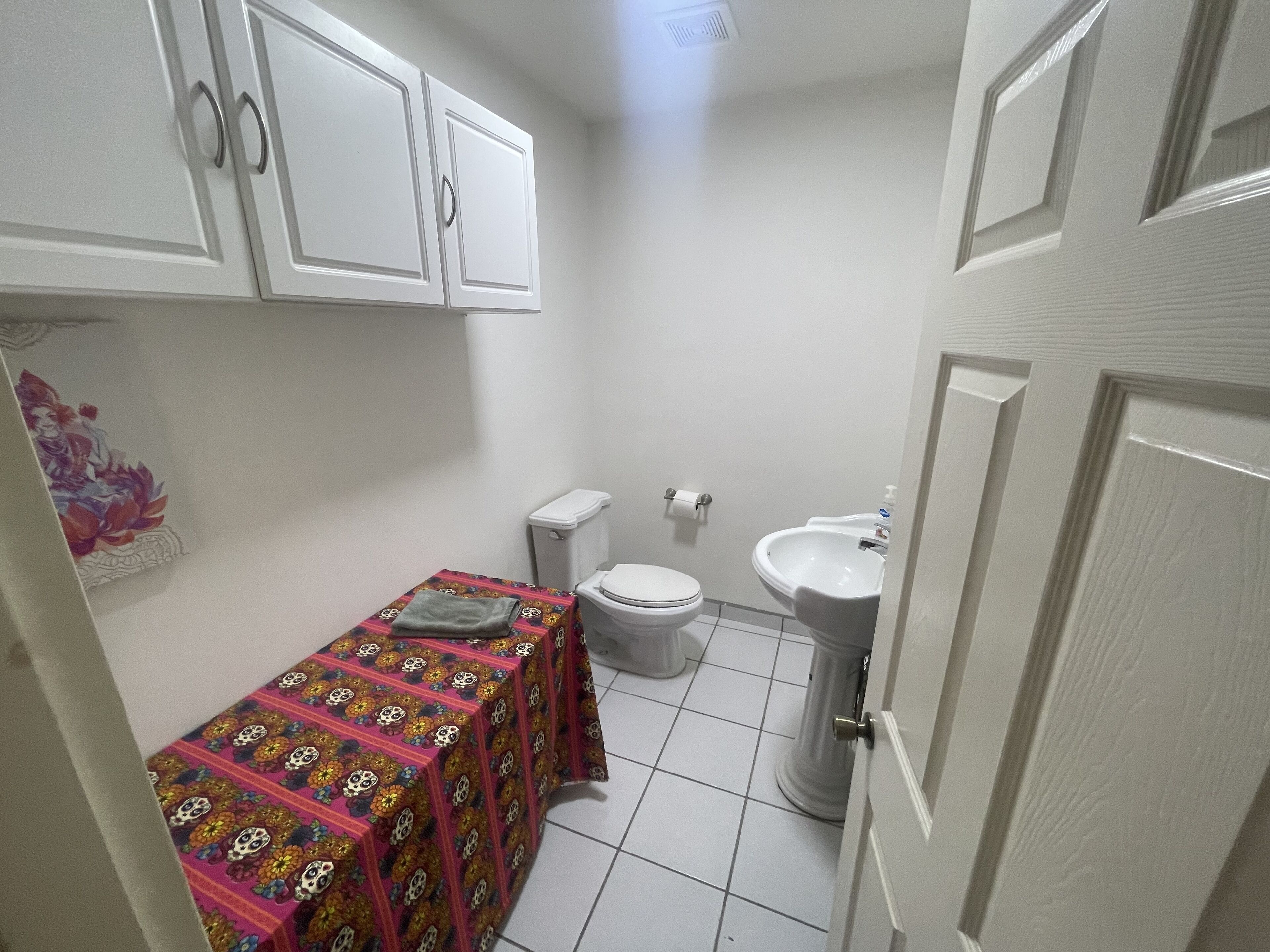 A small bathroom with a toilet, sink, and a table with a colorful tablecloth.