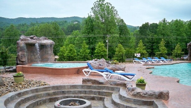 Un área de piscina con sillones de descanso, un jacuzzi y una fogata.